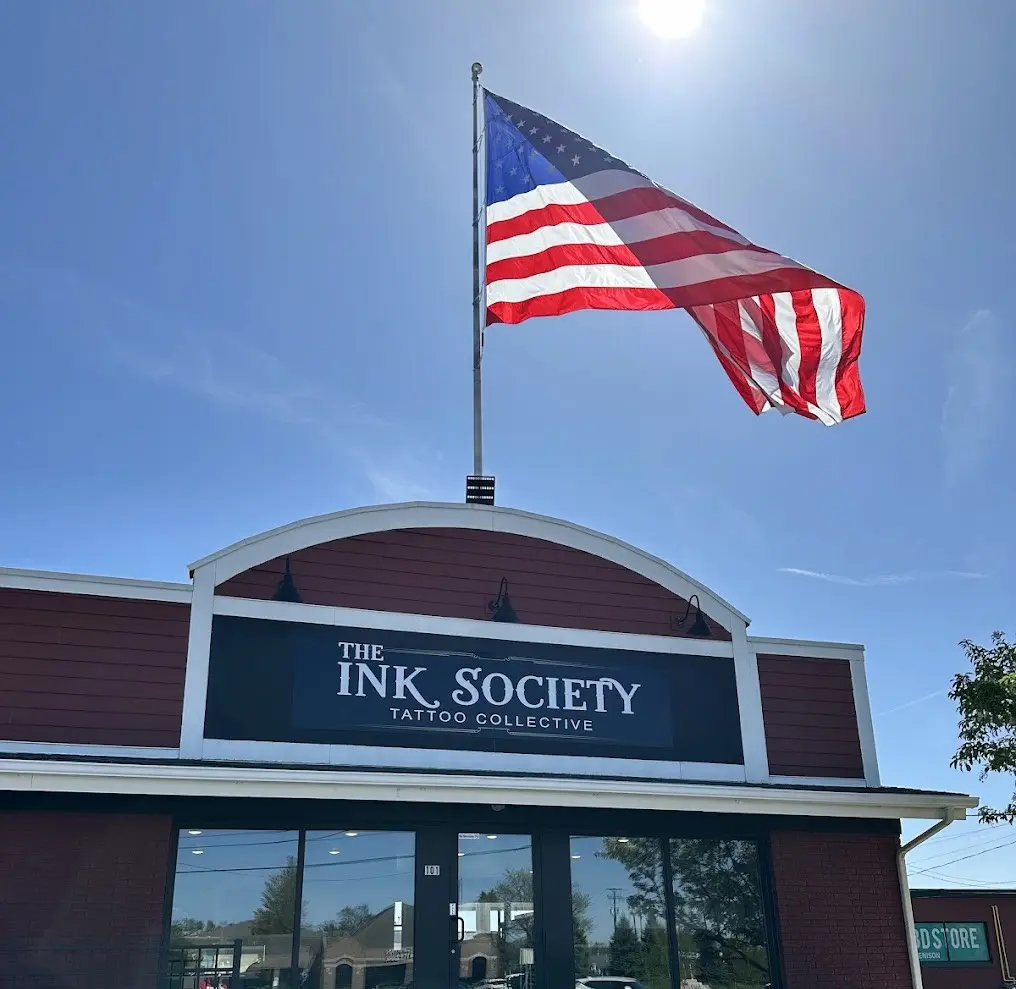 Storefront of The Ink Society on a sunny afternoon with large American Flag waving