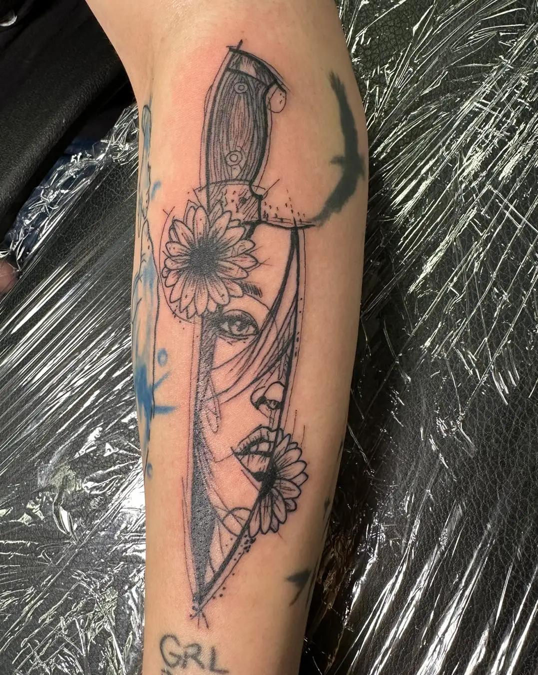 Black & white forearm tattoo of sunflowers, a knife, and a girl's face Black & white forearm tattoo of sunflowers, a knife, and a girl's face